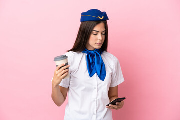 Airplane stewardess Brazilian woman isolated on pink background holding coffee to take away and a mobile