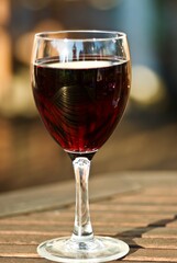 Glass of red wine on wooden table outdoors in the summer evening.