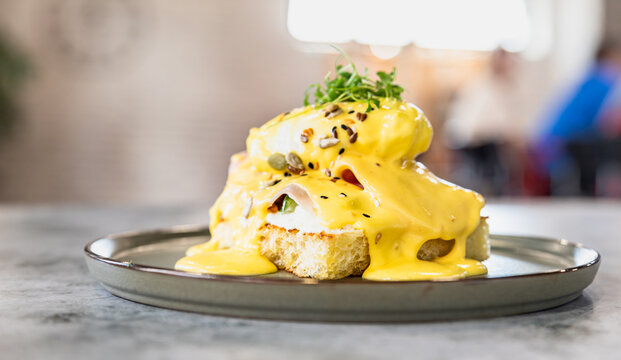Crispy toast with ham, poached egg, mashed avocado and hollandaise sauce decorated with microgreen