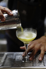 Fototapeta na wymiar barman vertiendo el licor de una coctelera en copa de coctel