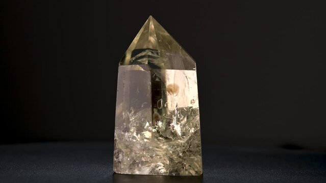 Smokey citrine point, rotating up close, with internal facets and prism effects.  Macro natural crystal on dark background.