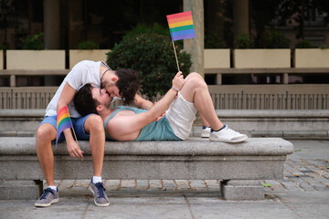 Obraz premium Two young men using the smartphone sitting in the street backwards. Gay couple.