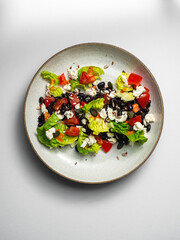 Black beans salad, with cheese, tomatoes, peppers, chia, herbs. On a ceramic plate, with a white  background