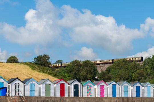 Colourful beach houses. Row of multi-coloured beach huts with steam train on stone viaduct against blue sky.