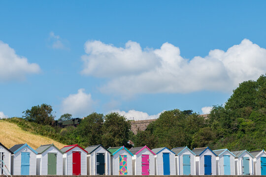 Colourful beach houses. Row of multi-coloured beach huts with steam train on stone viaduct against blue sky.