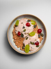 Breakfast Porridge with fruit, grapes , sunflower,  pumpkin seeds, yoghurt,  on a ceramic plate, with a white  background