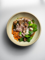 Pho soup - with beef, smoked tofu, carotts, pak choi, sesam, mushrooms, coriander, chili and rice noudels. On a ceramic plate, with a white  background