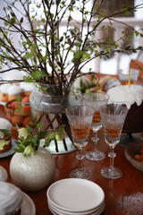Christian holiday, Easter. Baking with white icing with a candle. Easter cake. Festive table setting: flowers, glasses, colored eggs. Spring atmosphere, outdoor. Rustic. Background image, copy space