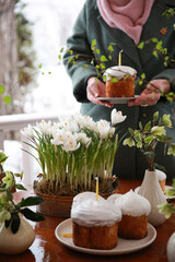 Christian holiday, Easter. Baking with white icing with a candle. Easter cake with hands. Festive table setting: flowers, glasses, colored eggs. Spring atmosphere, outdoor. Background image
