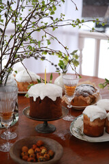 Christian holiday, Easter. Baking with white icing with a candle. Easter cake. Festive table setting: flowers, glasses, colored eggs. Spring atmosphere, outdoor. Rustic. Background image, copy space