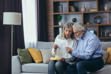 Angry frustrated document senior couple. Unhappy old family getting stressed. Serious older husband showing banking paper document bills taxes to confused elderly wife in home. Worried looking utility