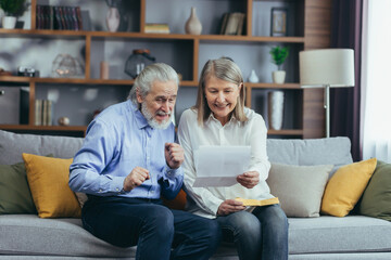 Senior gray haired family member receiving letter or document rejoicing sitting at home. Cheerful husband and wife retirees smiling while reading the good news. Old people watch. Joyful grandparents