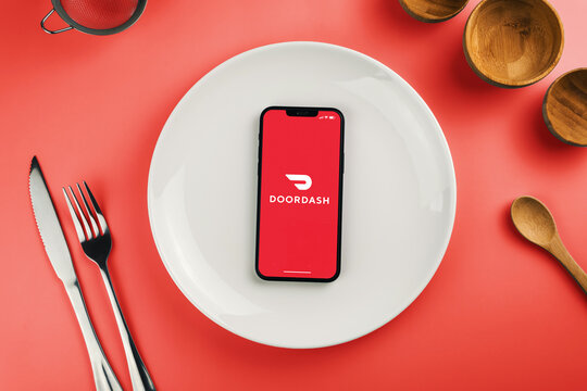 Doordash delivery app on smartphone screen on top of white plate. Beside cutlery and utensils. Waiting for delivery to eat the food. Rio de Janeiro, RJ, Brazil. April 2022