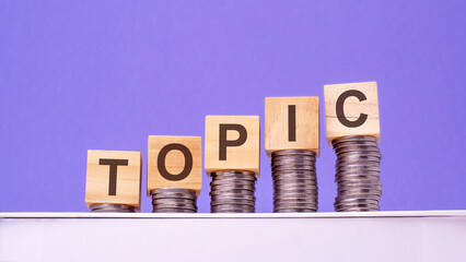 wooden cubes with the word Topic on money pile of coins, business concept