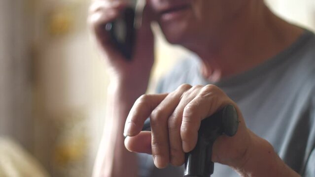 An elderly Caucasian man over 70 years old sits with a walking stick and communicates on the phone. Retiree in a nursing home talking on the phone.Selective focus, shallow depth of field