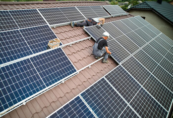 Men technicians building photovoltaic solar moduls on roof of house. Workers in helmets installing...