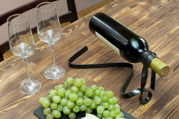 Obraz premium Elegant modern metal red white wine bottle holder on wooden table with glasses, brie cheese, grapes on black slate board, alcohol drink with snacks, flat lay top view close up