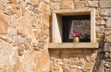 Janela em pedra no meio de paredes de pedras irregulares com vaso de flores e reflexo no vidro