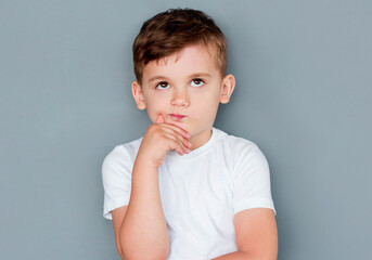 Emotional thinking little boy in casual outfit on gray background