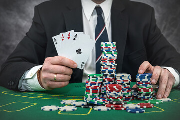 Stylish man in black suit holding play cards and poker chips in casino