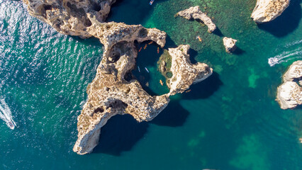 Aerial drone shot of kayaks and boats passing around magical Ponta da Piedade limestone cliffs. Exploring caves and tunnels of Lagos, Algarve, South of Portugal. Travel and adventure. Nomad life.  © stu.dio