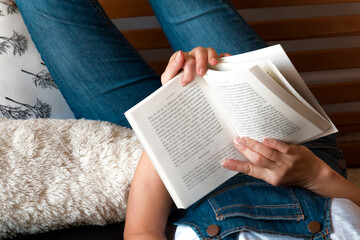 Close-up of woman hands holding a book while she is relaxing at the comfort of her home reading it