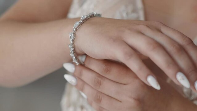 Stylish woman bride in wedding dress puts silver bracelet with gems on wrist in room closeup slow motion. Accessories for marriage ceremony