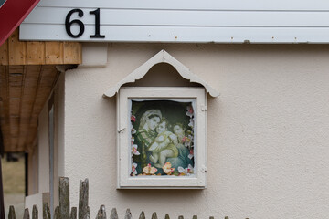 Fototapeta na wymiar Gieraltow, Lower Silesia, Poland - April 2, 2022: An icon depicting the baby Jesus in the arms of the Virgin Mary and an angel on the facade of a house in the village of Geraltow