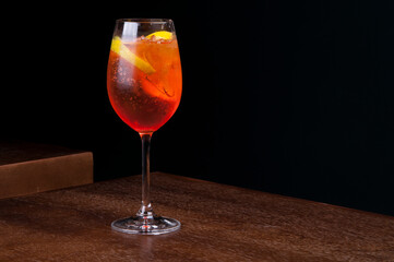 aperol spritz glass with sparkling ice on wooden table with dark background front view corner
