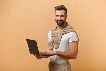 Positive cheerful man with beard holding laptop and looking at camera with smile, satisfied with...