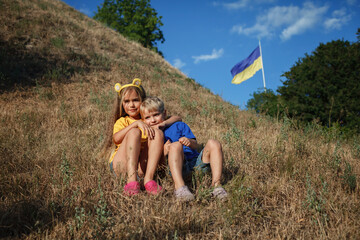 Small patriots, girl in yellow and boy in blue, sitting near the biggest national flag of Ukraine....