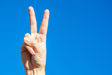 Symbol of peace. Raised fingers up. Palm on a background of blue sky