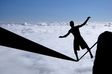 Silhouette of young man balancing on slackline high above clouds and mountains. Slackliner balancing on tightrope beautiful colorful sky and clouds behind, highline silhouette.