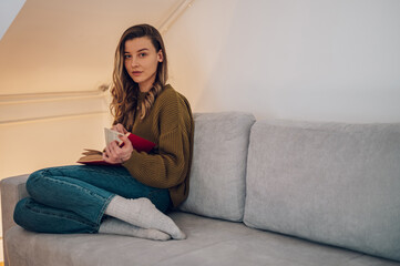 Obraz premium Woman reading a book while sitting on the couch at home