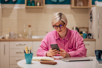 Short haired woman using smartphone in the kitchen at home