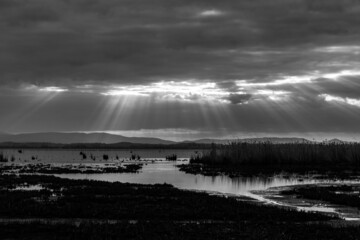 Sunrays at near sunset, with dark clouds in the background, above Trasimeno lake, Umbria, Italy