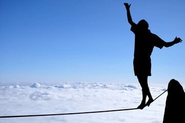 Silhouette of young man balancing on slackline high above clouds and mountains. Slackliner balancing on tightrope beautiful colorful sky and clouds behind, highline silhouette.