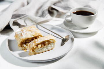 Apple charlotte with cottage cheese cream on a porcelain plate and a cup of tea on the table.