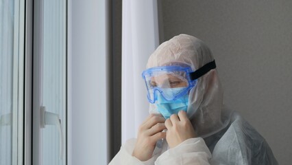The doctor puts on a protective suit and a mask with goggles before working with those infected with the coronavirus. Danger of infection from patients with severe infection. Medic at work.