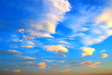 Blue sky with many soft little clouds colored in pink and orange pastel shades during sunset in...