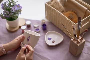 Womens hands paint a white flower ceramic pot on the table