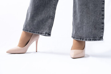 Women's legs in elegant patent leather high-heeled beige shoes. Gray wide leg jeans. Side view