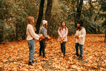 Four young women staying preparing to throw maple leaves in the air. Having fun, enjoy promenade in orange autumn park