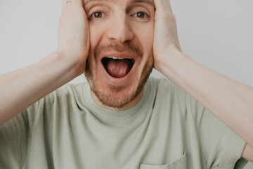 Handsome young man over grey wall shocked screaming with open cover mouth mock up, unexpected shocking news