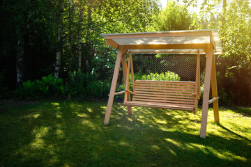 Wooden summer swing on the green grass in the garden. Garden decoration. Landscape design.Summer...