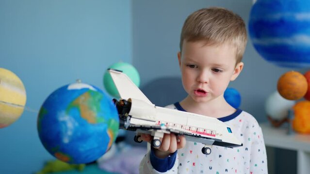Cute boy is playing with toy space shuttle, flying in space among planets of solar system. Child playing at home with space shuttle flying in space of solar system. Cosmonautics Day on April 12.
