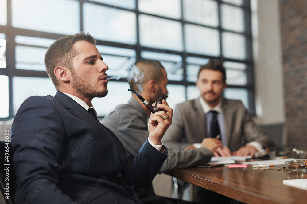Poster taking a break from the brainstorming. shot of a businessman smoking a pipe during a meeting at the 