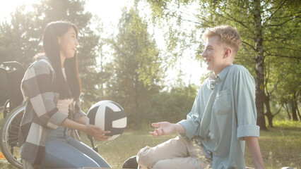 On the foreground in a good weather two best friends are sitting on the plaid in the public park...