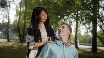 Fototapeta premium A pretty young asian girl is stroking her boyfriend's shoulders, they are talking together in the public park and looking to each other, slow motion