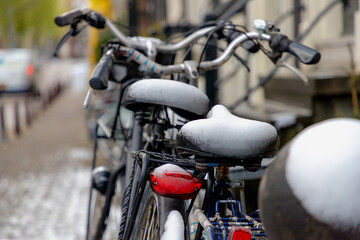 Selective focus of snow covered bicycle seat parked on the street, Heavy and snowy day in winter with white fluffy snowflakes, Cycling is a common mode of transport in Holland, Amsterdam, Netherlands.